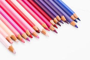 Multi-colored pencils lie on a white table, the violet range of colors photo