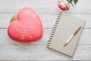 Heart shaped pink mousse cake on table with rose and notepad. photo