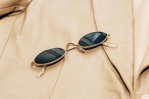 Gold-rimmed sunglasses on the texture of a brown leather jacket, genuine soft leather photo