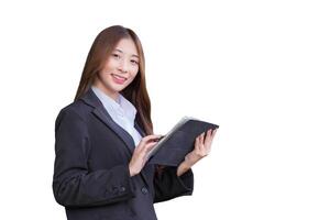 Asian professional business young woman in dark blue suit smiles happily stand with confidence and look at camera while she works and holds tablet front office while isolated on white background. . photo