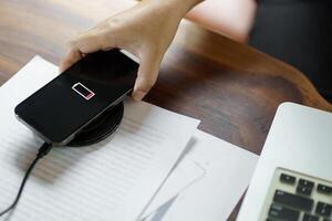 Charging mobile phone battery with wireless charging device in the table. Smartphone charging on a charging pad. Mobile phone near wireless charger Modern lifestyle technology concept photo