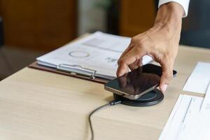 Charging mobile phone battery with wireless charging device in the table. Smartphone charging on a charging pad. Mobile phone near wireless charger Modern lifestyle technology concept photo