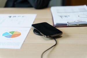 Charging mobile phone battery with wireless charging device in the table. Smartphone charging on a charging pad. Mobile phone near wireless charger Modern lifestyle technology concept photo