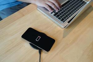 Charging mobile phone battery with wireless charging device in the table. Smartphone charging on a charging pad. Mobile phone near wireless charger Modern lifestyle technology concept photo
