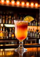 A delicious Tequila Sunrise cocktail drink on a polished Mahogany bar top in a cozy bar with various alcohol bottles out of focus in the background. photo