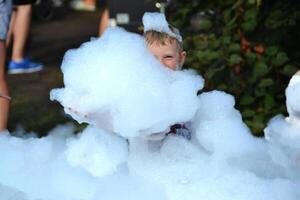 happy little boy with foam on his head, in wet clothes at a foam party photo
