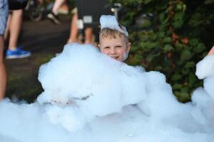 happy little boy with foam on his head, in wet clothes at a foam party photo