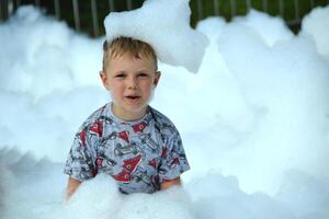 happy little boy with foam on his head, in wet clothes at a foam party photo