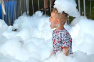 happy little boy with foam on his head, in wet clothes at a foam party photo