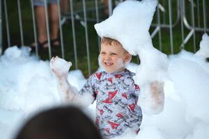 happy little boy with foam on his head, in wet clothes at a foam party photo