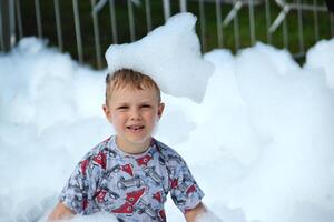 happy little boy with foam on his head, in wet clothes at a foam party photo
