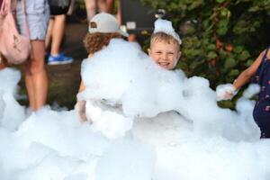 happy little boy with foam on his head, in wet clothes at a foam party photo