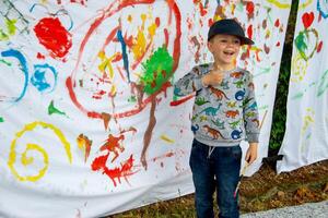 Young child creating a colourful abstract painting with a paintbrush on a sheet photo