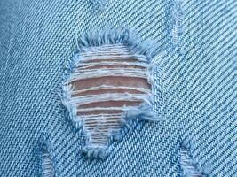 Hole and Threads on Denim Jeans. Ripped Destroyed Torn Blue jeans background. Close up blue jean texture photo