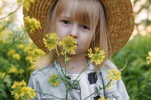 Blonde girl in a field with yellow flowers. A girl in a straw hat is picking flowers in a field. A field with rapeseed. photo