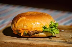 a beef cheese burger filled with meat, tomato sauce, mayonnaise, and lettuce on a cutting board and picnic style cloth that looks delicious and tempting to make hungry stomachs photo