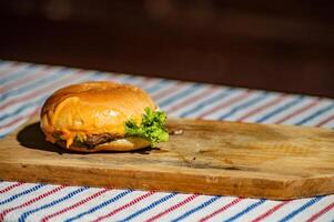 a beef cheese burger filled with meat, tomato sauce, mayonnaise, and lettuce on a cutting board and picnic style cloth that looks delicious and tempting to make hungry stomachs photo