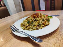 table manner a plate of fried rice on a wooden table with a spoon on the right and a fork on the left of the plate photo