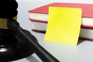 Judge's gavel with yellow note and red books on white background. photo