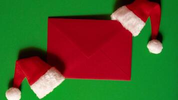 Zoom in out Santa hat with empty paper card note envelope on green background. Copy space for your text. Mock up for advertisement. Holiday Christmas composition. Minimalistic greeting card. Creative video