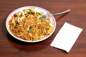 Fried noodle with chicken and vegetables in a white bowl on a wooden table. After edits. photo