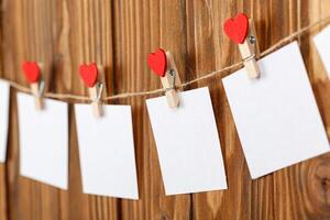 white pieces of paper on clothespins with a heart on a wooden background photo