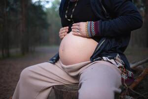 a pregnant woman sits on a log in the forest and hugs her tummy photo
