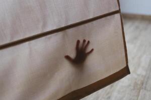A child's hand presses against a curtain, casting a mysterious and gentle shadow silhouette photo