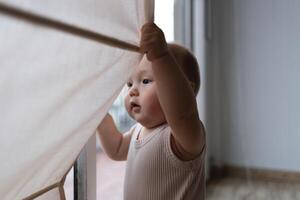 A curious baby pulls the curtain aside, discovering the world beyond the window with wonder photo