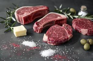 Various raw beef steaks with herbs, salt, and butter ready for cooking on a dark background photo