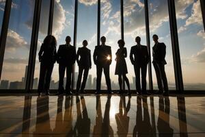 Professional business team silhouetted against office windows with city skyline backdrop at sunset photo