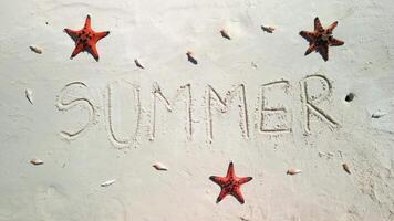 SUMMER written on the sand on a tropical beach with red starfish and shells. video