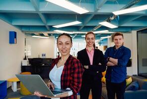A young team of business professionals poses for a startup office portrait, exuding confidence and ambition, with one woman holding a laptop, symbolizing innovation and collaboration in photo