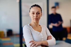 Portrait of a business woman in a creative open space coworking startup office with crossed arms. Successful businesswoman standing in office with copyspace. Associates work in the background photo
