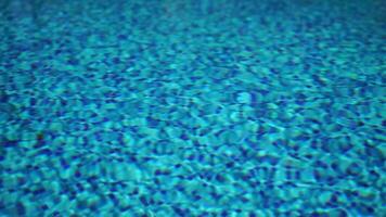 Pool water background with wavy clear fresh water. Calm rest on sunny day. Abstract reflections on the surface of the water with texture of bright blue pool tiles. Turquoise water surface. Slow motion video