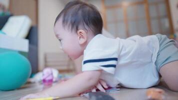 Happy asian baby crawls in the room playing with blue rubber air ball next to cozy sofa. Boy Toddler playing in the house and learns how to crawl, child development skills, learning age preschooler video