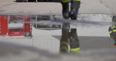 A reflective scene captures a firefighter heading into a dangerous firefighting mission, his image mirrored on the water's surface as he holds a fire hose, symbolizing bravery and readiness in the video