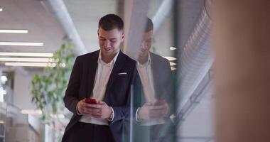 A busy businessman in a modern corporate hallway showcases his multitasking skills while using a smartphone to manage his hectic work schedule and stay connected with the fast-paced business world video