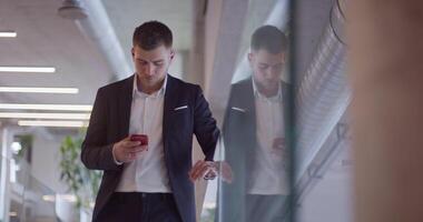 A busy businessman in a modern corporate hallway showcases his multitasking skills while using a smartphone to manage his hectic work schedule and stay connected with the fast-paced business world video
