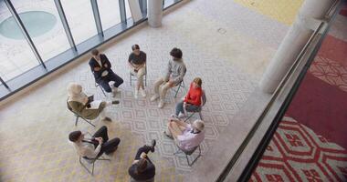 Top view of a diverse group of young business entrepreneurs gathered in a circle for a meeting, discussing corporate challenges and innovative solutions within the modern confines of a large video