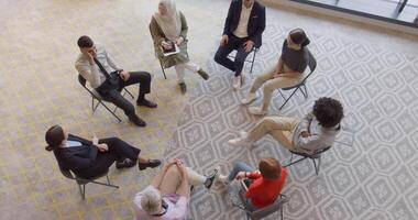 Top view of a diverse group of young business entrepreneurs gathered in a circle for a meeting, discussing corporate challenges and innovative solutions within the modern confines of a large video