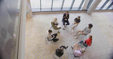 Top view of a diverse group of young business entrepreneurs gathered in a circle for a meeting, discussing corporate challenges and innovative solutions within the modern confines of a large video