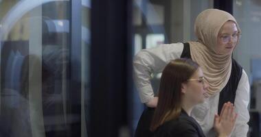 A diverse group of businesswomen, one of whom wears a hijab, collaborates while focusing on a laptop, engaging in discussions and problem-solving, showcasing professionalism, teamwork, and effective video