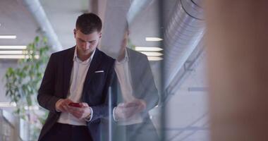 A busy businessman in a modern corporate hallway showcases his multitasking skills while using a smartphone to manage his hectic work schedule and stay connected with the fast-paced business world video