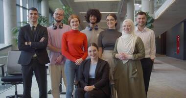 A diverse group of young business professionals stands confidently and looks into the camera in a modern business center, symbolizing ambition, diversity, and a forward-thinking corporate culture video