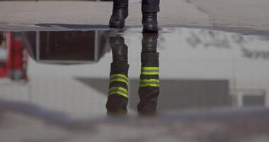A reflective scene captures a firefighter heading into a dangerous firefighting mission, his image mirrored on the water's surface as he holds a fire hose, symbolizing bravery and readiness in the video