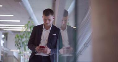 A busy businessman in a modern corporate hallway showcases his multitasking skills while using a smartphone to manage his hectic work schedule and stay connected with the fast-paced business world video