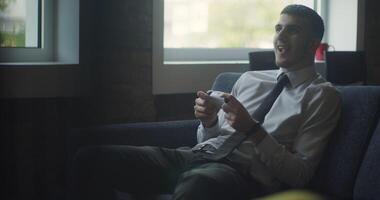 A business company's director takes a break from work in a modern office and indulges in gaming, using a joystick to play games on a TV, combining leisure and relaxation with a dash of office video