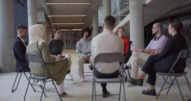 A diverse group of young business entrepreneurs gathered in a circle for a meeting, discussing corporate challenges and innovative solutions within the modern confines of a large corporation video