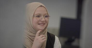 In a modern office, a Muslim entrepreneur wearing a hijab sits confidently and diligently works on her computer, embodying determination, creativity, and empowerment in the business world video